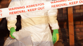 A worker wearing protective clothing while clearing asbestos from an old attic.